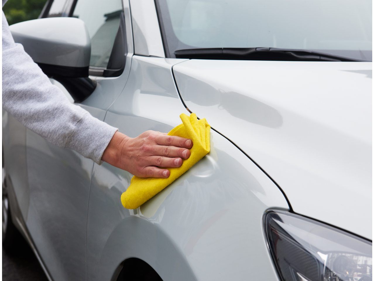 Uma mão limpa um carro branco com um pano amarelo, parte do kit de reparação de mossas PARKSIDE.