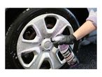 A person cleaning a car wheel with a spray bottle of wheel cleaner, creating purple foam.