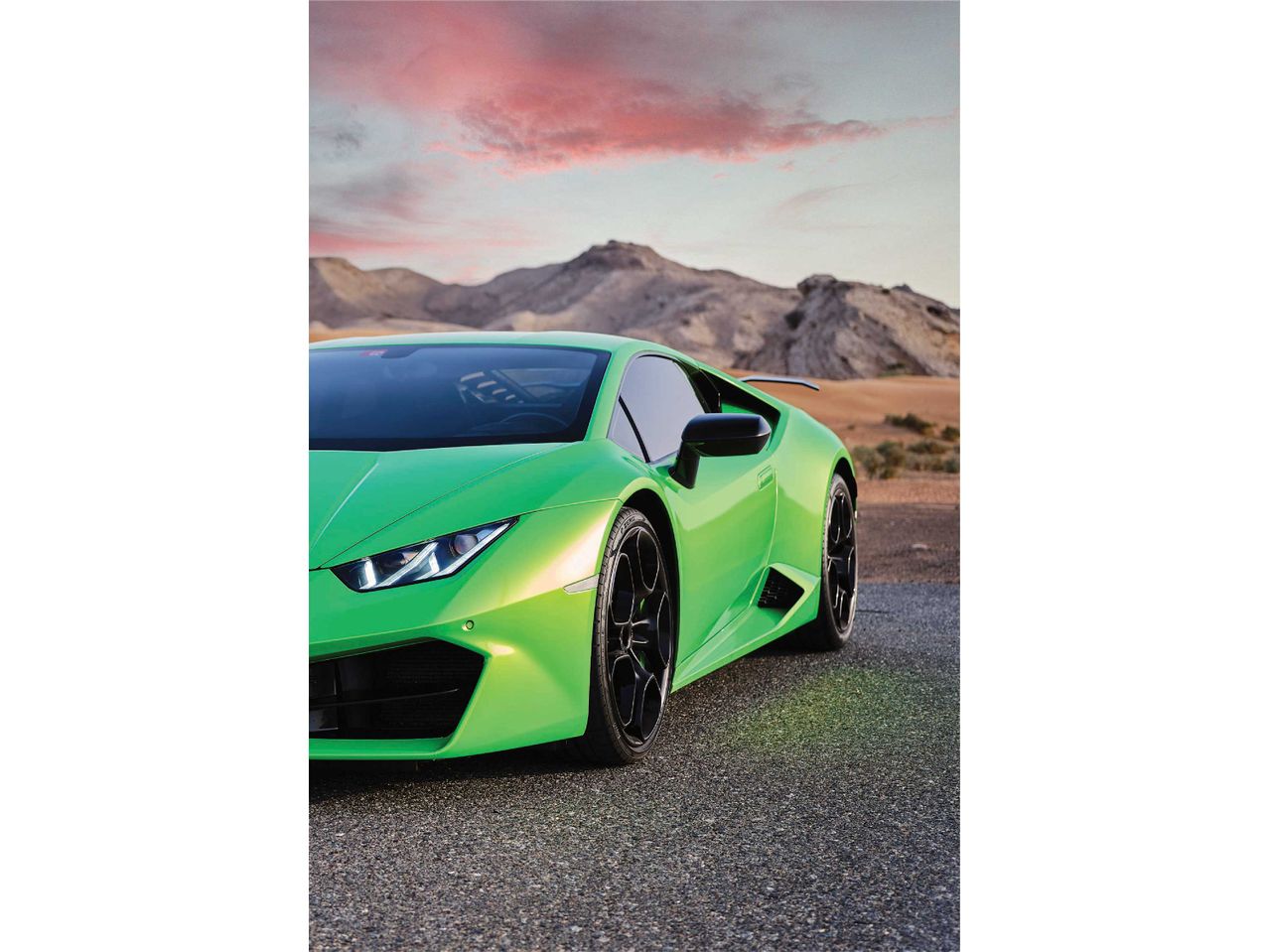 Zöld Lamborghini Huracán egy sivatagi úton, hegyekkel és rózsaszín égbolttal a háttérben.