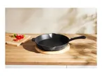 A black cast iron skillet on a wooden cutting board with chopped red peppers.