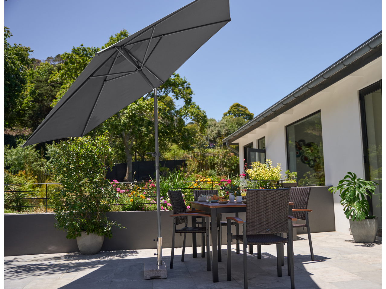 Siv vrtni senčnik z mizo in stoli na sončni terasi.