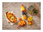 A bottle of clementine juice, a glass of juice, and a dish of clementines and dessert on a wooden table.