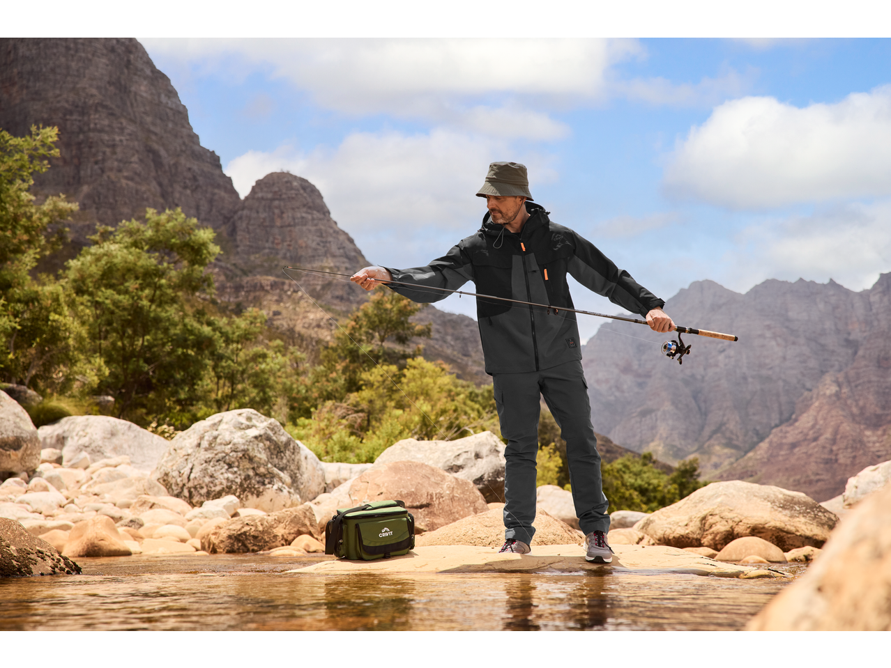 Άνδρας ψαρεύει με τσάντα αλιευτικού εξοπλισμού CRIVIT στην όχθη του ποταμού.