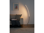 A modern arc floor lamp illuminates a living room with a beige sofa and a framed print.