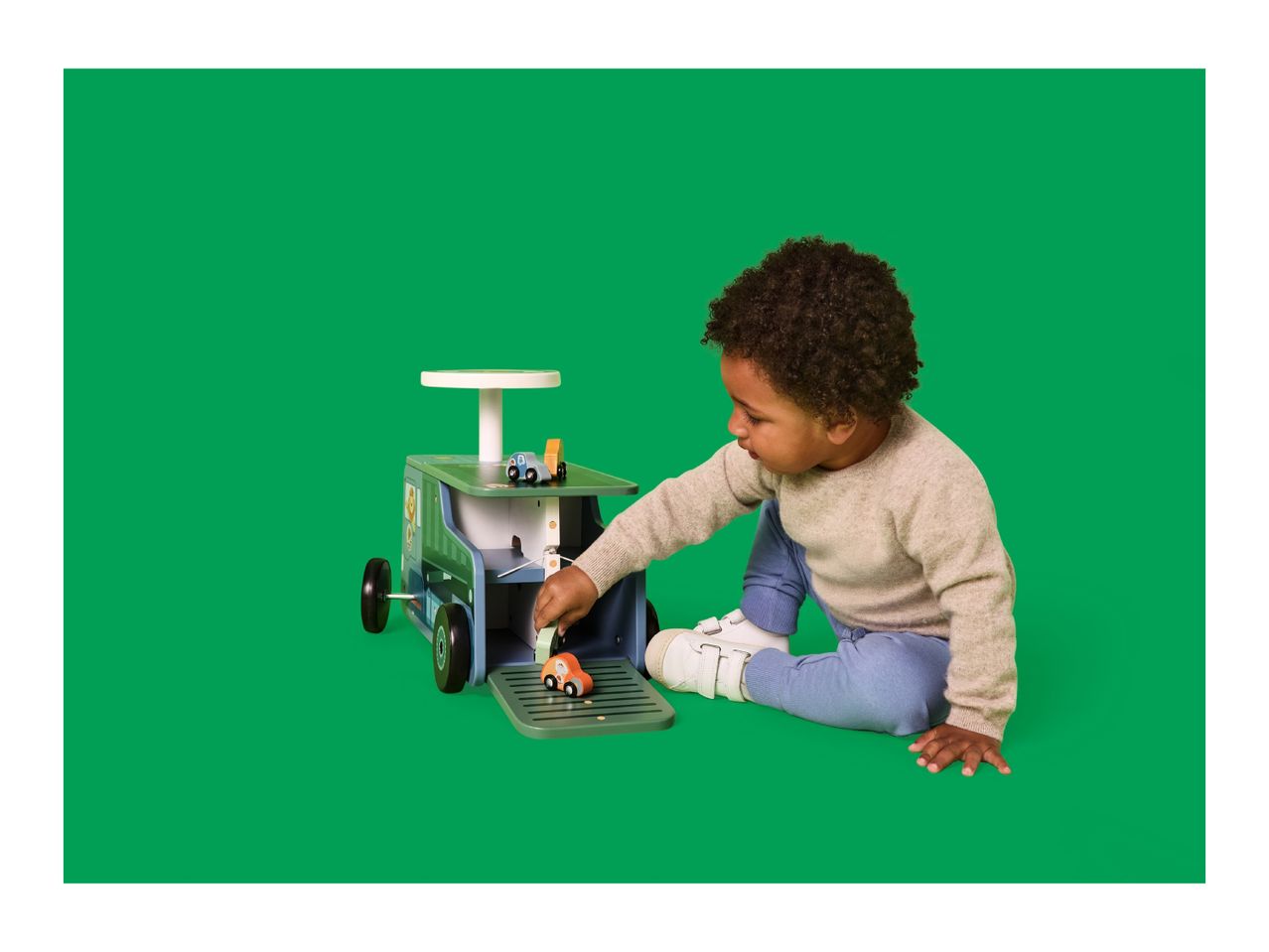 A child playing with a wooden toy car carrier and small wooden cars on a green background.