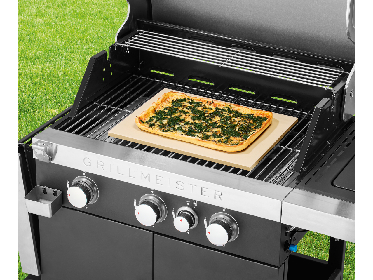 Grillmeister, grătar cu gaz negru cu pizza pe o piatră de copt, pe fundal de iarbă verde.