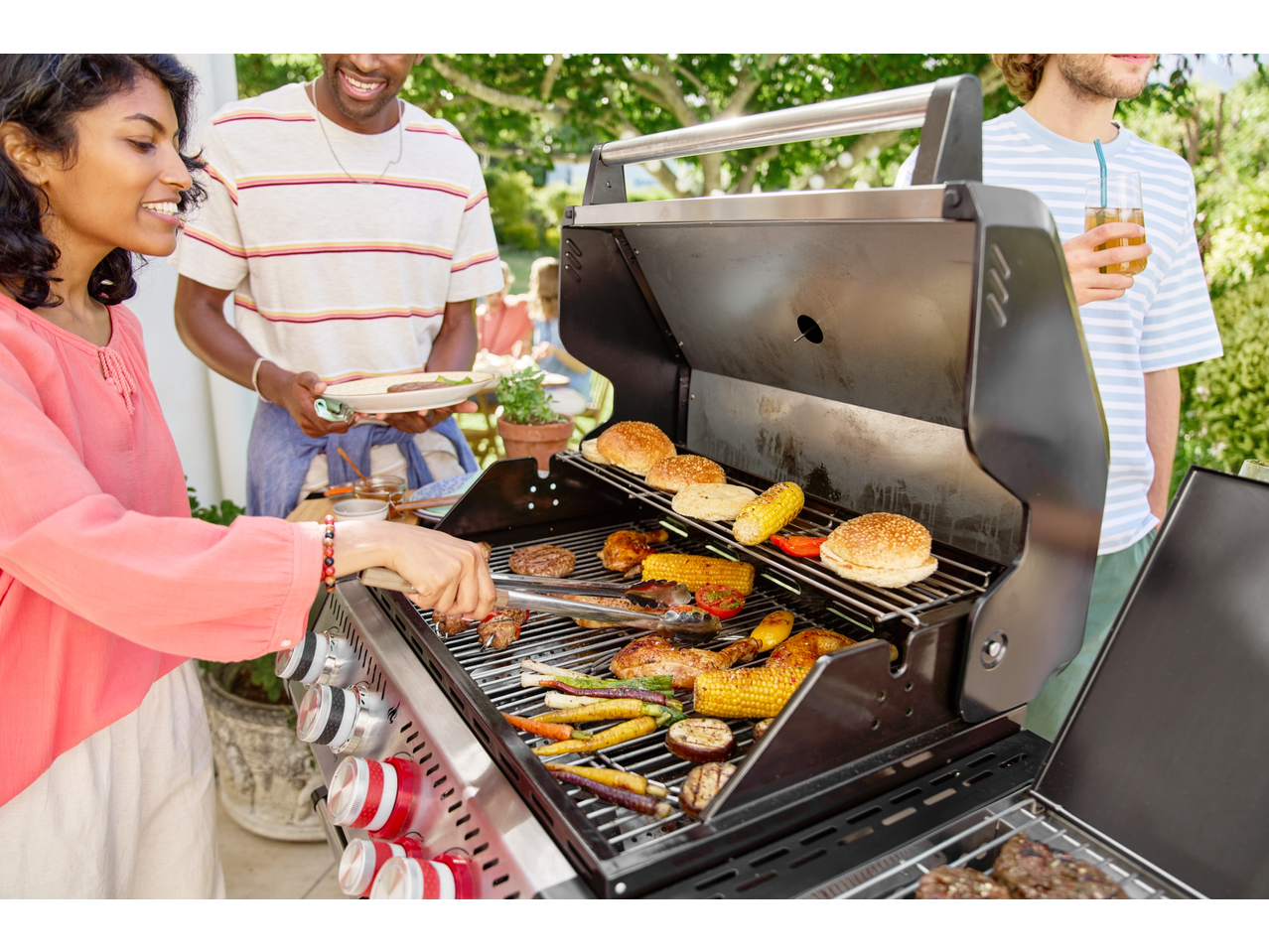 Friends grilling burgers, chicken, and vegetables on a Grillmeister 4 Burner Gas Barbecue.