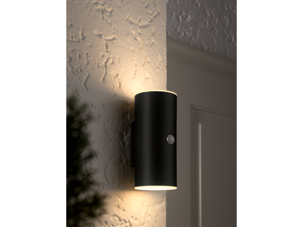 Schwarze zylindrische Wandleuchte, die eine strukturierte Wand nach oben und unten beleuchtet.