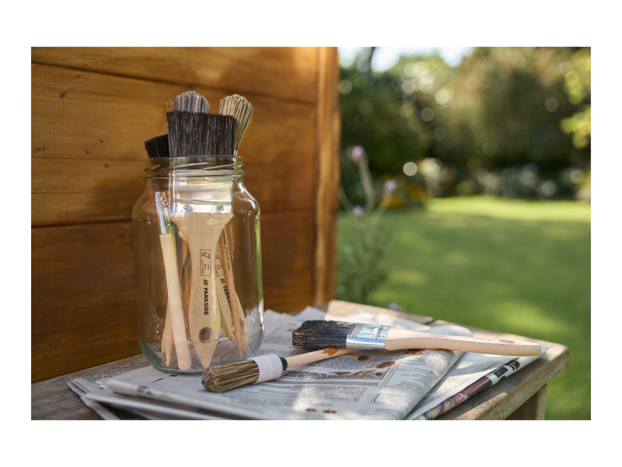 Paintbrushes in a jar and on newspaper, with a garden in the background.