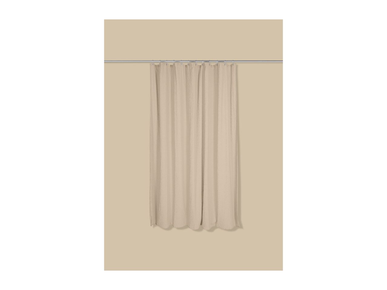 Beige shower curtain with a textured pattern, hanging from a silver rod.