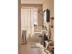 Bagno moderno e minimalista con doccia a soffitto, lavabo e mobiletto.