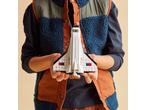 A child in a fleece vest holds a white toy spaceship.