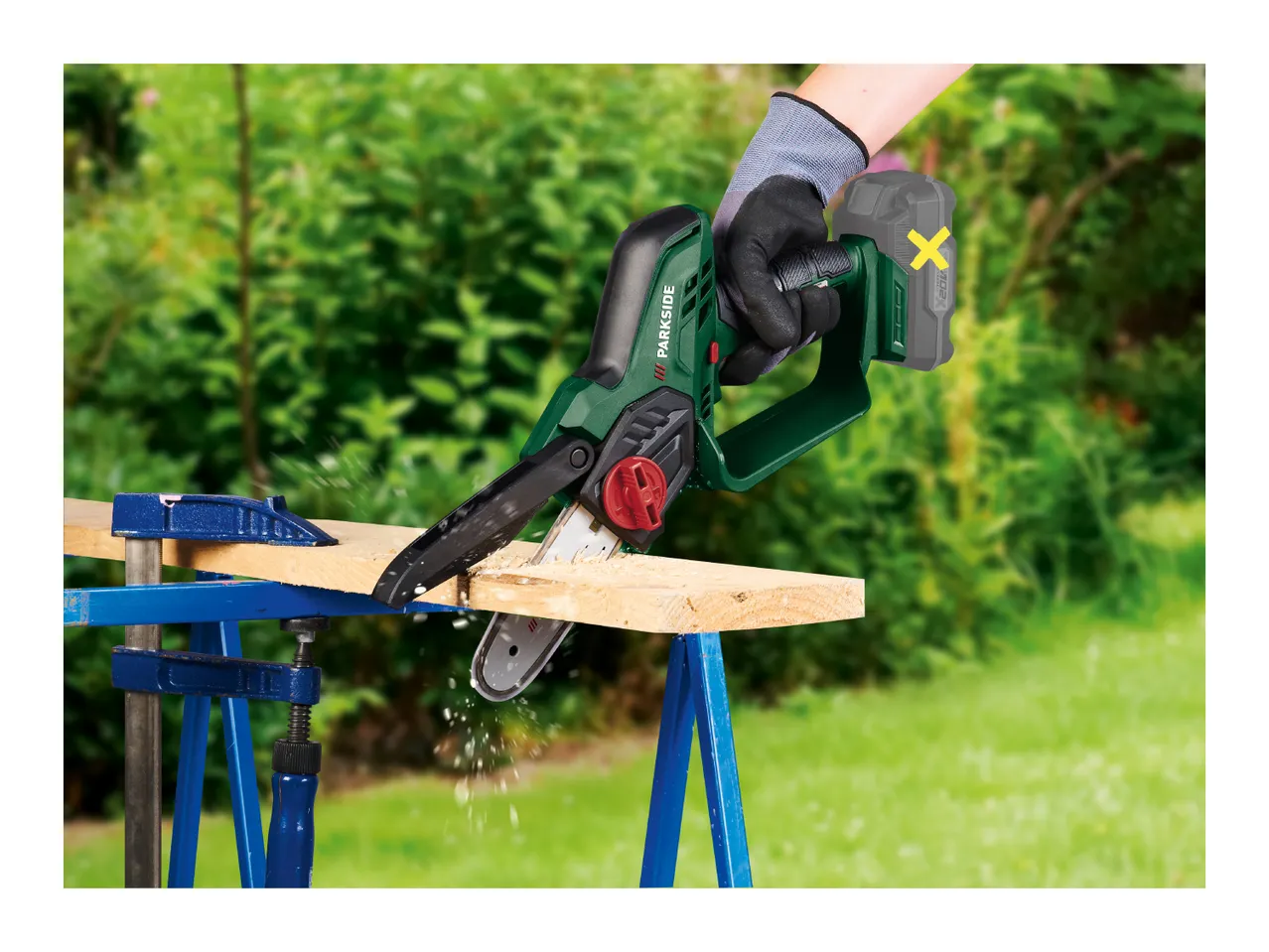 A person using a cordless mini chainsaw to cut a wooden plank outdoors.