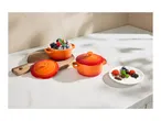 Orange mini cocottes with dessert and fresh berries on a white marble surface.