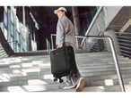 A woman carries a black Samsonite suitcase up a staircase.