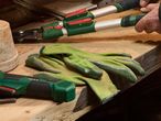 Gardening tools including loppers, gloves, and a power tool on a wooden surface.