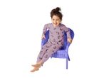 A happy child in unicorn-patterned pajamas sits in a purple wicker chair.