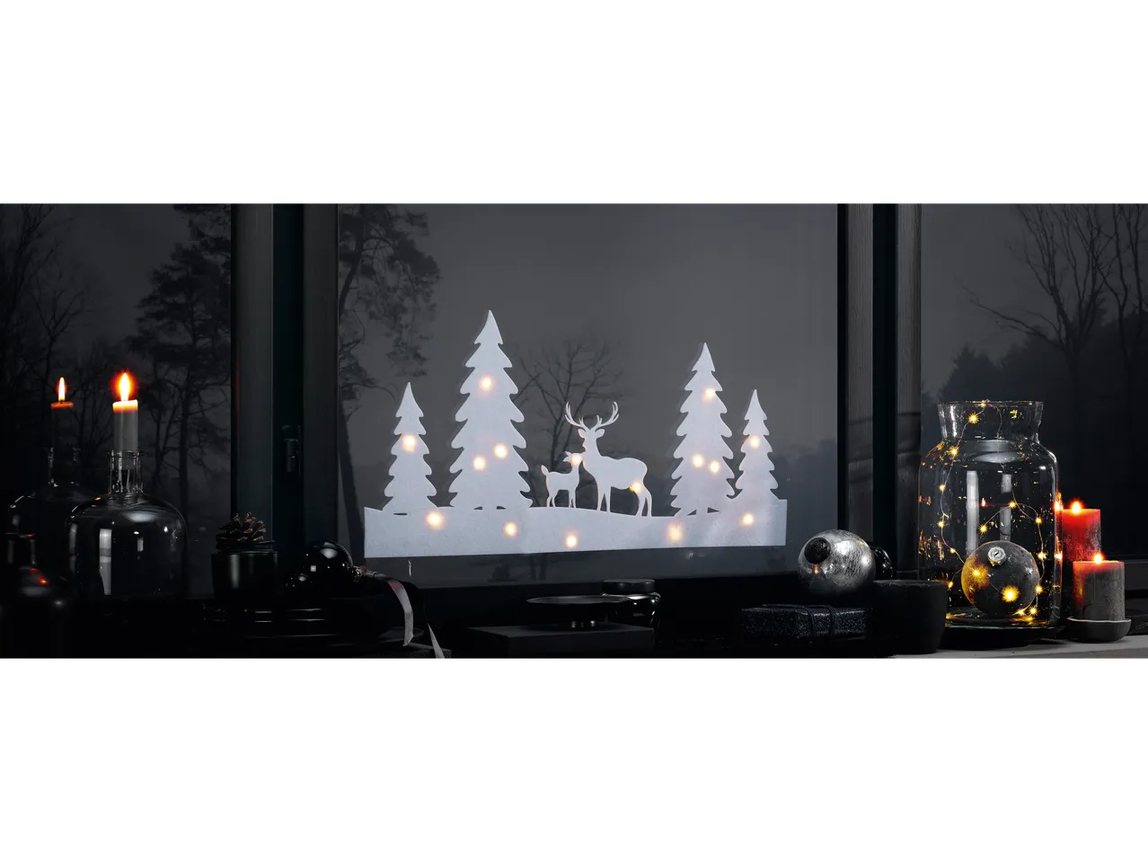 LIVARNO home LED Window Decoration with deer and trees, surrounded by candles and ornaments.