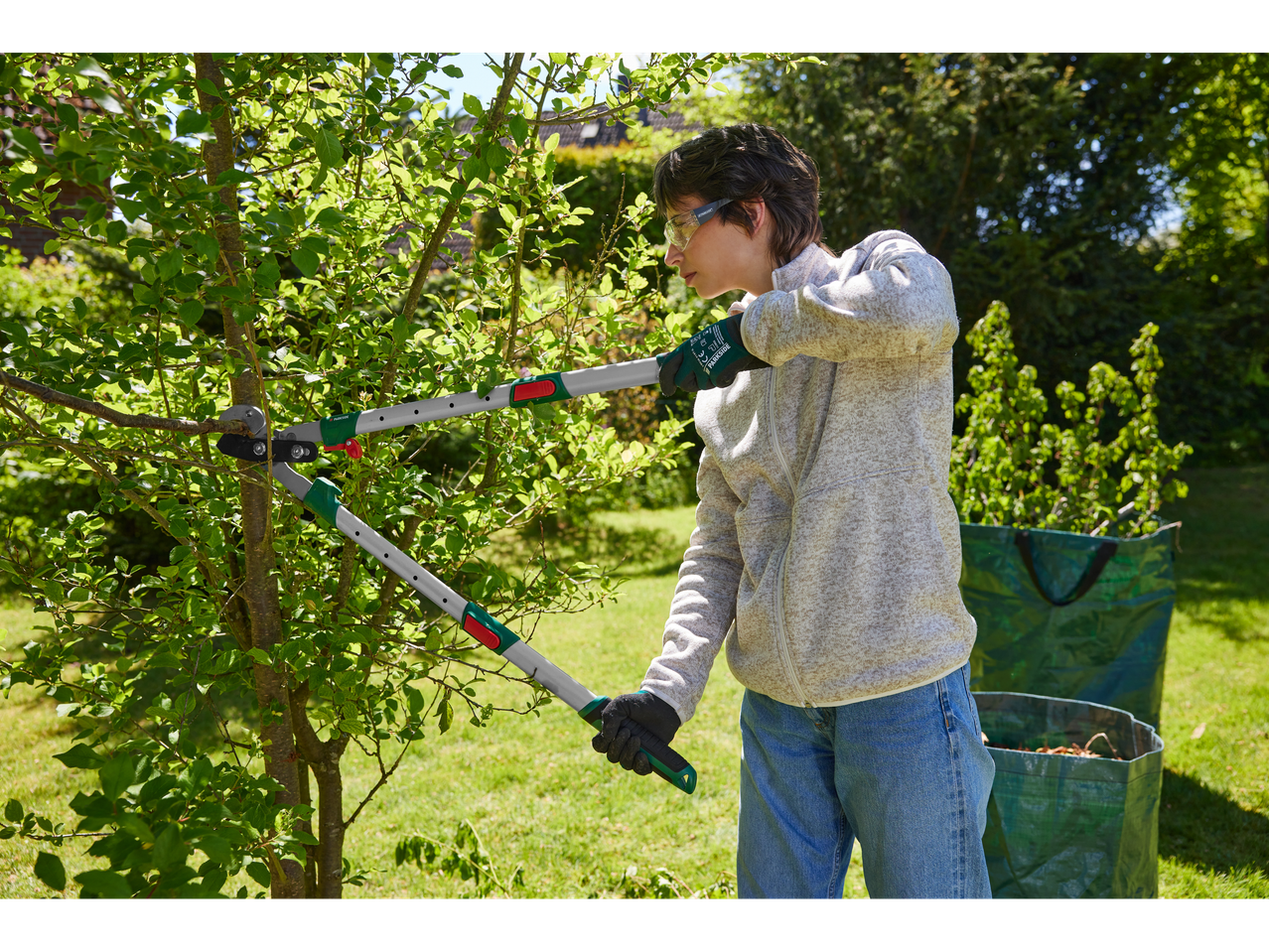 A person uses Parkside telescopic loppers to prune a tree branch in a garden.