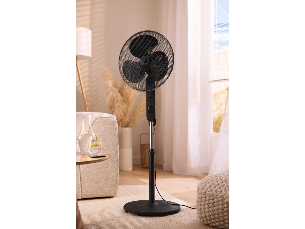 Black pedestal fan in a bright living room with a sofa, side table, and window.