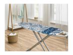 Ironing board with blue and white leaf pattern, clothes rack, and laundry basket in a bright room.